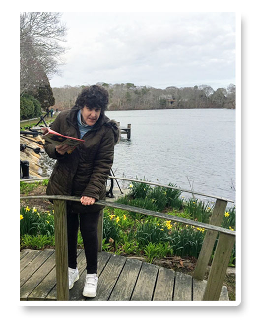 Erica standing on a wooden deck by a lake, smiling and holding a tablet.